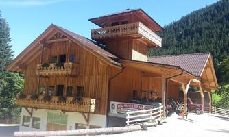 A beautiful wooden house in the mountains with balconies and an upper observation tower. Surrounded by green trees and a clear mountain landscape.