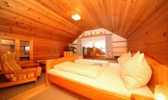 A cozy bedroom with wood paneling and a large bed. There are comfortable chairs and windows with curtains that let in natural light.