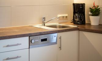 A modern kitchen with a sink, dishwasher, and a coffee machine. The furniture is in light colors and the lighting creates a cozy atmosphere.