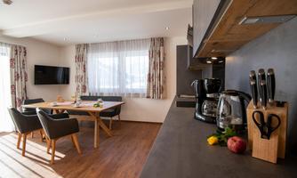 A modern kitchen with a dining area and large windows. The furniture is stylish and the atmosphere is bright and inviting.