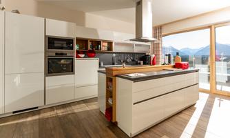 A modern kitchen with a cooking island in the center.  
Large windows provide plenty of daylight and a view of the mountains.