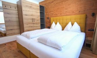 A modern bedroom with a cozy double bed and bright pillows. The room has wooden walls and a large mirror.
