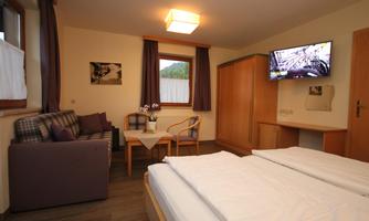 A cozy room view with two beds, a sofa, and a table. There is a television on the wall and windows with curtains.