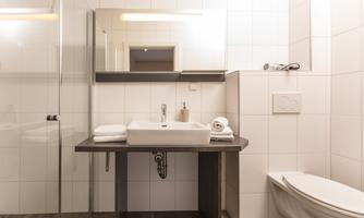 A modern bathroom with a clear shower cabin and a stylish sink. The walls are designed with white tiles, and there are fresh towels.