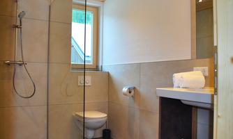 A modern bathroom with a glass shower and a toilet. Towels are neatly placed on the sink.