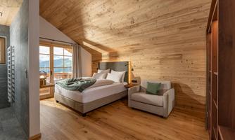 A cozy bedroom with wood paneling and a large window that offers a view of the mountains. The room contains a comfortable bed and a cozy armchair.