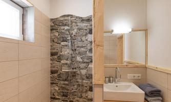 A modern bathroom with a stone shower and bright tiles. Towels are lying on the sink, and a mirror is attached to the wall.