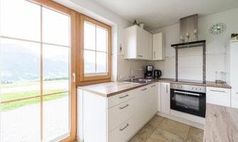 A modern kitchen with white cabinets and a large window front. The view overlooks a beautiful landscape with mountains in the background.