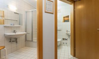 A bright bathroom with a shower and sink. The walls are tiled and there are wooden details on the doors.