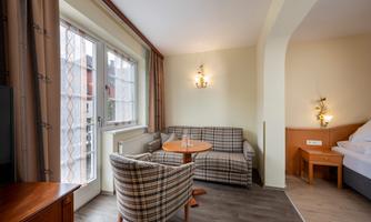 A cozy room with a sofa, two armchairs, and a round table. Large windows let in a lot of light.
