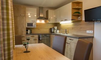 A modern kitchen with wooden surfaces and an open dining area. It includes appliances such as a stove, a microwave, and a kitchen table with chairs.