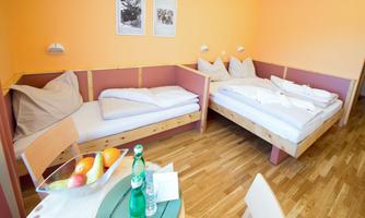 A cozy room with two beds and cheerful orange walls. Fresh fruit and water bottles are on the table.