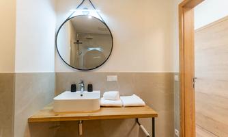 A modern bathroom with a round mirror and an elegant sink. White towels are neatly stacked on a wooden shelf.