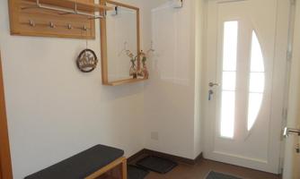 A bright entrance area with a wooden bench and a coat panel. The door has a modern design and lets in a lot of light.