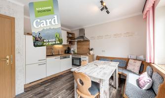 A modern kitchen with wooden details and a cozy dining area. In the foreground, the Schladming-Dachstein Card is visible.
