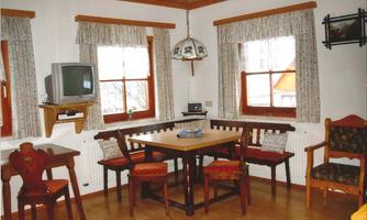 A cozy dining area with a table and chairs, surrounded by windows with curtains. The room has a rustic charm with a wooden floor and a ceiling lamp.