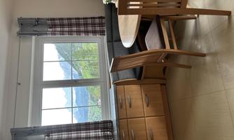 A cozy dining area with a round table and wooden chairs. A beautiful panoramic landscape with mountains can be seen through the window.