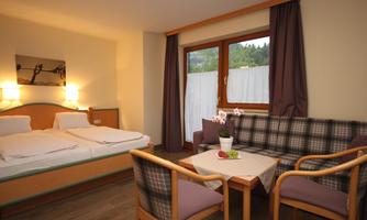 A cozy hotel room with a double bed and a seating area. Large windows let in plenty of daylight.