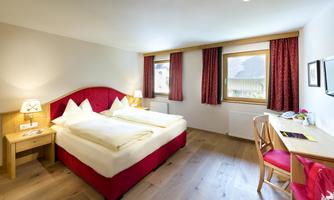 A cozy hotel room with two beds, hardwood floor, and a large window. The decor is designed to be modern and welcoming.