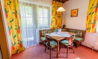 A cozy dining area with a round table and colorful curtains. The rooms appear bright and inviting through the window and the decoration.
