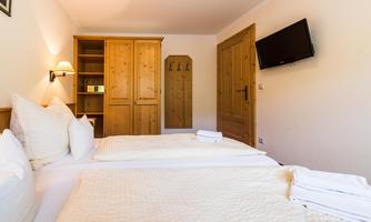 A cozy room with two beds and bright walls. There is a wardrobe, a television, and a warm atmosphere.
