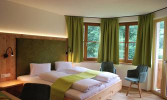 A modern bedroom with wooden furniture and large windows. The curtains are green and the room feels bright and inviting.