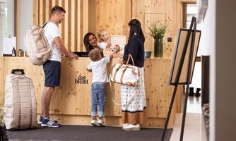 A family is standing at the reception of a hotel. The staff member greets them warmly, while the children are curious.