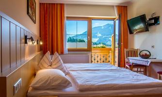 A cozy hotel room with two beds and wooden decor. The view from the window shows a beautiful mountain landscape.