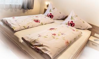 A cozy bedroom with a double bed and floral-patterned bedding. The windows let in natural light, creating an inviting atmosphere.