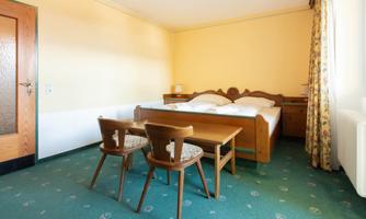 A simple room with two beds and a table. The walls are painted in warm shades of yellow, and there are two wooden chairs.