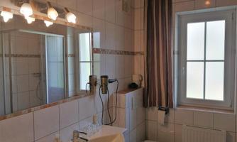 A modern bathroom with a sink, a mirror, and a window. The walls are tiled, and there is a shower as well as a toilet.