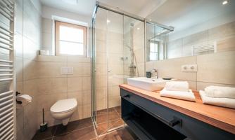 A modern bathroom with a glass shower and a wooden washbasin. Soft towels are neatly arranged on the table.