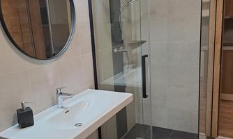 A modern bathroom with a large glass shower cabin and an elegant sink. The room features bright tiles and a round mirror.