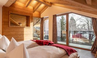 A cozy bedroom with wood paneling and large windows. The red ceiling adds a warm accent and provides a view of the nature outside.