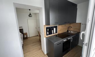A modern kitchen with dark cabinets and wood accents. The space is bright and open, with a view of the adjacent room.