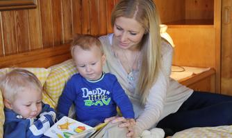 A mother is reading to her two small children in a cozy room. The children are sitting on the bed and are looking at the book with interest.