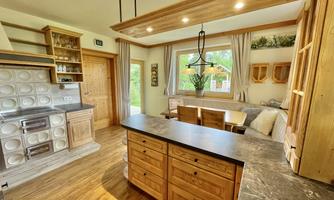 A modern kitchen with wooden shelves and a cooking island. Large windows let in plenty of daylight and offer a view outside.
