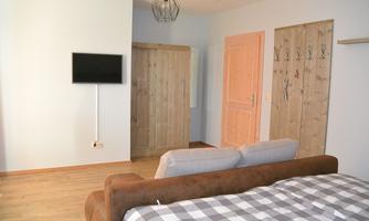 A modernly furnished room with a cozy sofa and a television on the wall. The wooden doors and the light wall color create an inviting atmosphere.