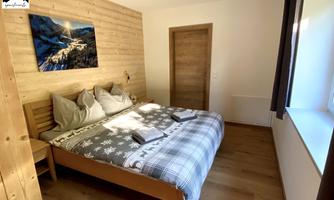 A cozy bedroom with a double bed and wood-paneled walls. There is also a window with a view of nature and a modern painting on the wall.