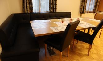 A dining room with a large table and a cozy corner bench. Black chairs surround the table, and curtains create an inviting atmosphere.