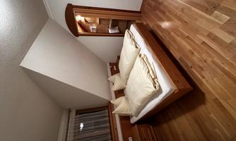 A cozy bedroom with a double bed and wooden furniture. The room has natural light through a window and a warm, inviting atmosphere.