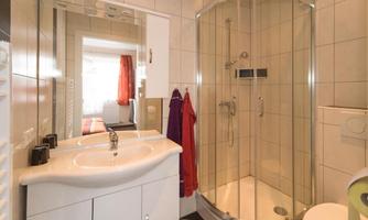 A modern bathroom with a shower cabin and a sink. The walls are tiled, and there is a large mirror.