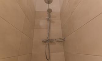 A modern shower with tiled walls and a handheld showerhead. The space is bright and simply designed.