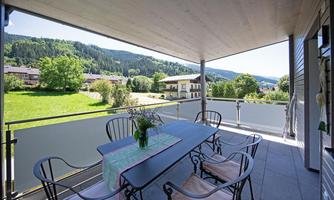 A cozy balcony with a table and chairs. In the background, a green landscape with trees and hills can be seen.
