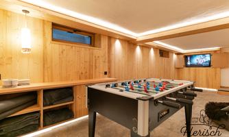 A cozy room with wooden walls and a table football game. Soft lighting and a television create a relaxed atmosphere.