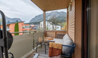 A cozy balcony with a view of the mountains and a modern seating area. The space is decorated with a ceiling and two wicker lamps.