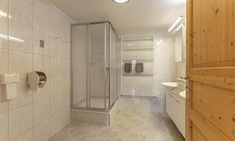 A modern bathroom with a shower cubicle and bright tiles. There is a sink unit and a wooden cabinet for additional storage.