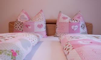 A cozy bedroom with pink striped pillows and heart-patterned bedding. The atmosphere is warm and inviting.