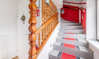An inviting hallway with a wooden staircase and a decorative railing. The walls are designed in warm colors, and the carpet adds a cozy atmosphere.