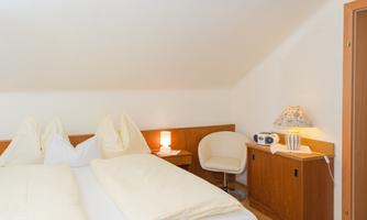 A cozy bedroom with a double bed and two pillows. On the side, there is an armchair and a small table with a lamp.